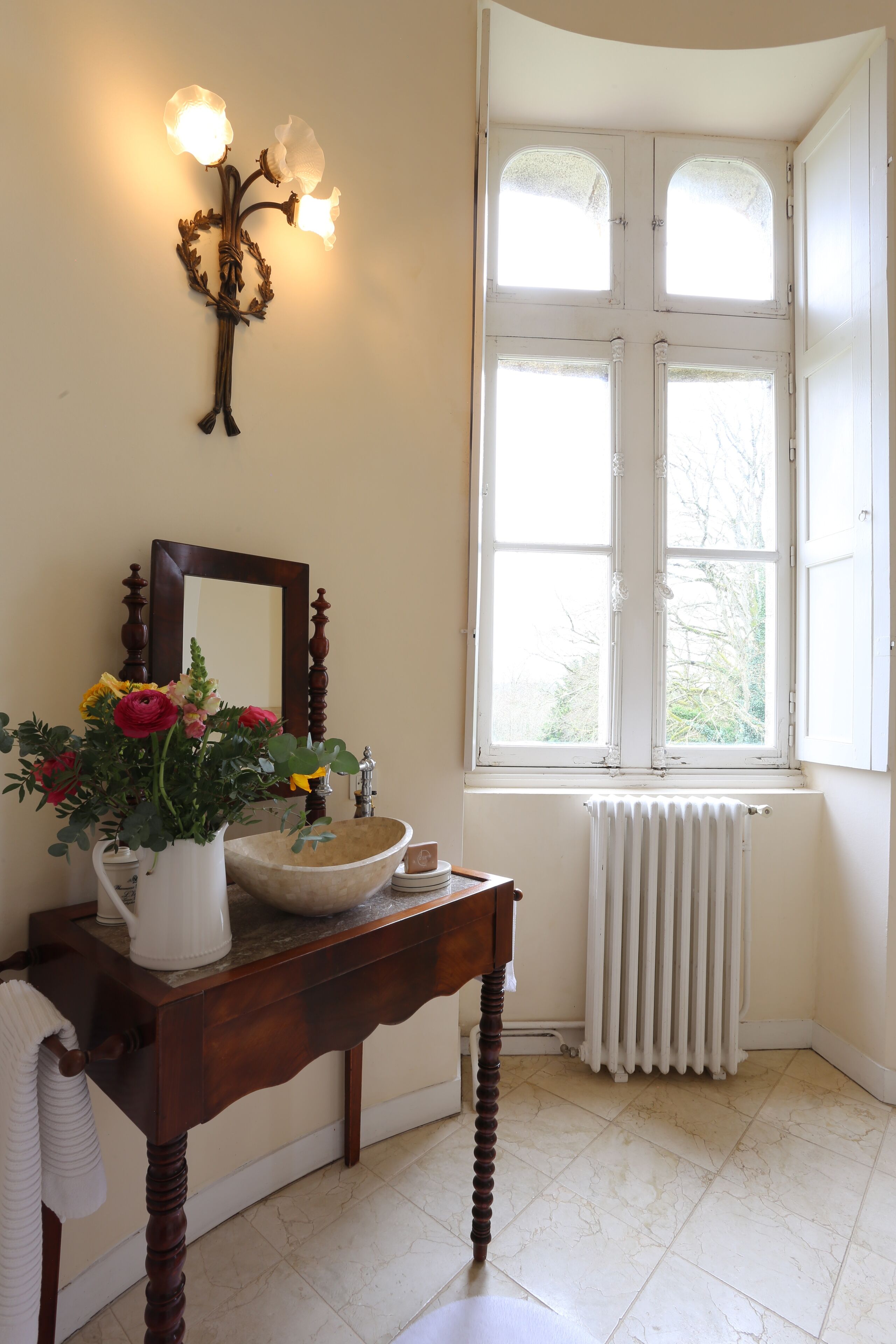 A bathroom with a wooden vanity, a white sink, a mirror, and a window with white shutters.