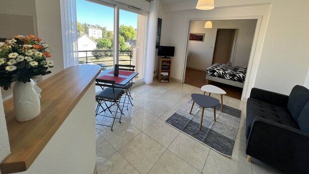 Una sala de estar moderna con comedor, sofá, televisor y balcón con vista al vecindario.