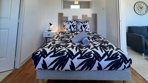 Un dormitorio con una cama, una mesita de noche, una lámpara, un espejo y un reloj en la pared.