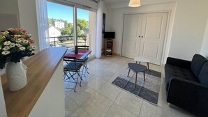 Una sala de estar moderna con sofá, una mesita y televisor. Hay un balcón con vistas a edificios y árboles.