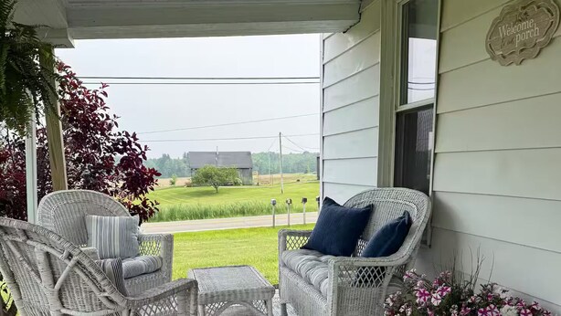 A porch with wicker furniture, a welcome sign, and a flower arrangement. - Charming 3-bedroom farmhouse with AC, WiFi in quaint Austinburg (Austinburg)