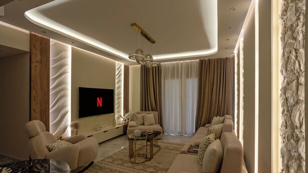 A modern living room with a flat-screen TV, comfortable seating, and a decorative ceiling light.