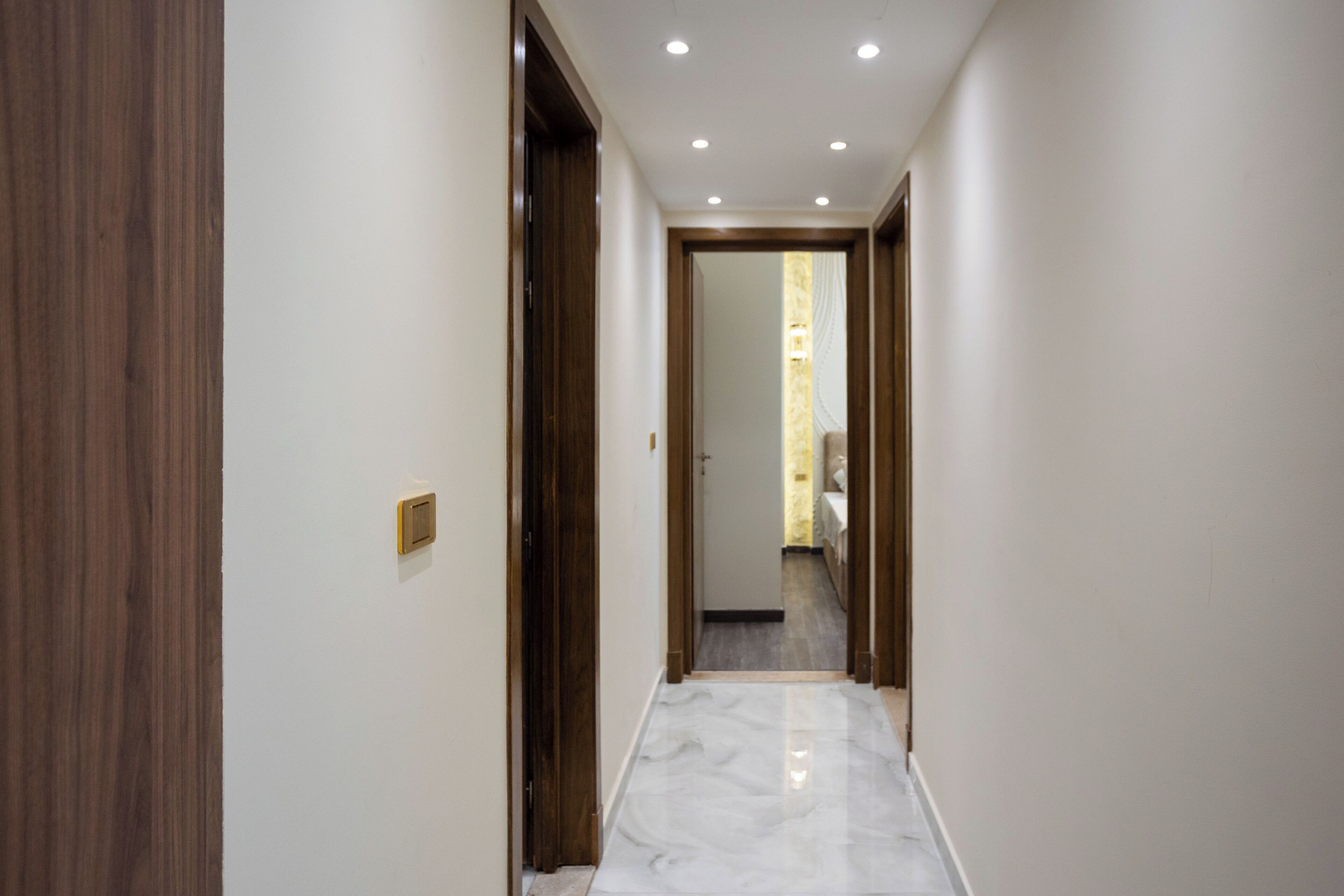 A hallway with wooden doors, a marble floor, and recessed ceiling lights.
