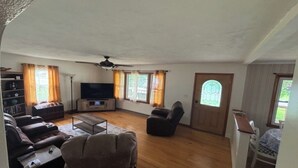 A spacious living room with a flat-screen TV, comfortable seating, a ceiling fan, and large windows with curtains. - Charming 3-bedroom Country Porch Home with AC, WiFi in Welcoming Town of Dayton (Dayton)