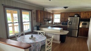 A kitchen with wooden cabinets, a central island, a dining table with chairs, and a refrigerator. - Charming 3-bedroom Country Porch Home with AC, WiFi in Welcoming Town of Dayton (Dayton)