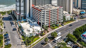 A multi-story hotel with a parking garage, located near a beach with a view of the ocean.