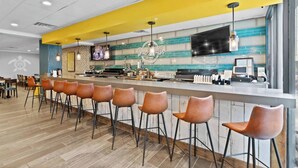 A modern bar area with a yellow accent wall, a flat-screen TV, and a bar counter with stools.