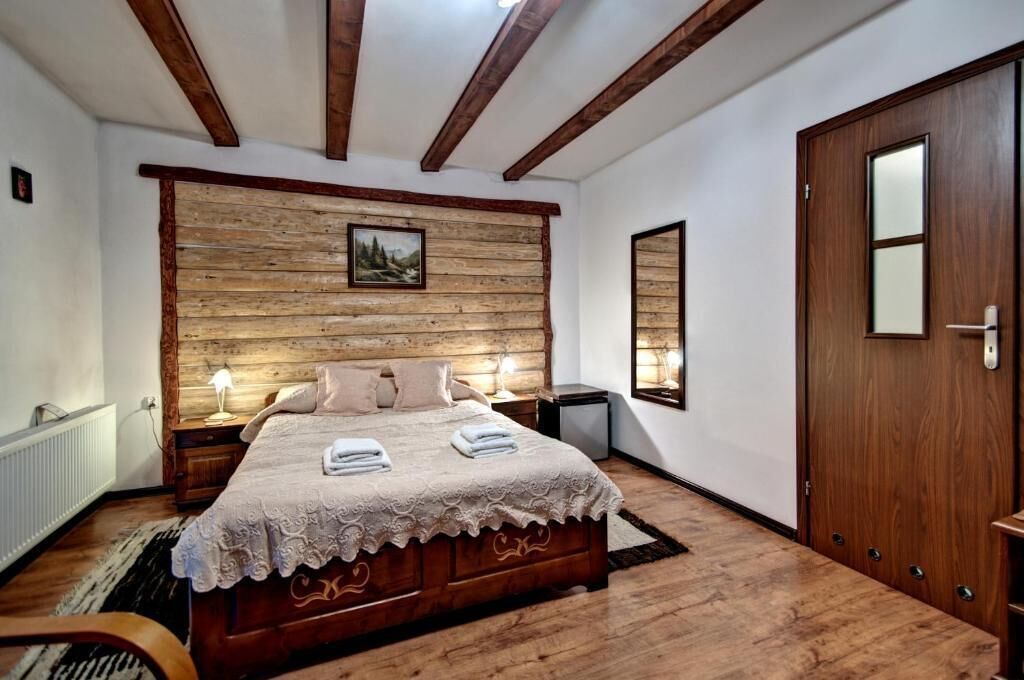 A wooden-framed bedroom with a bed, bedside lamps, and a door.