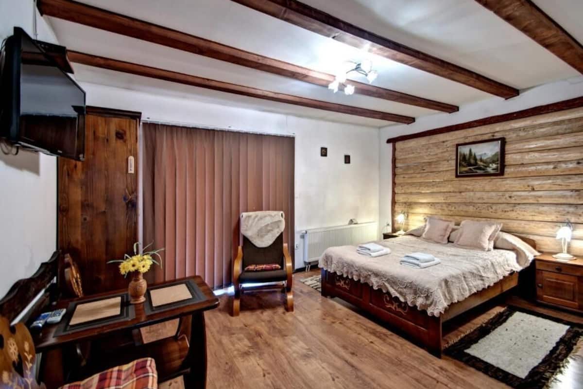 Un dormitorio con cama de madera, una silla, un escritorio, televisión y ventana con persianas.