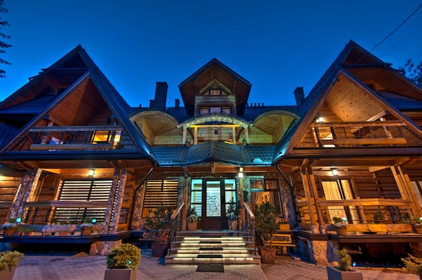 A large, multi-story wooden building with a prominent central entrance, multiple balconies, and a stone facade.