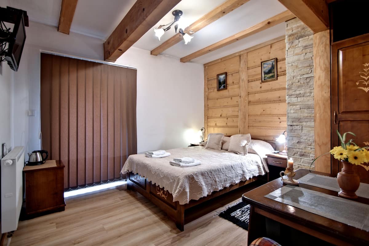 Un dormitorio con cama de madera, mesita de noche, cómoda, radiador, ventana con persianas y techo de madera.