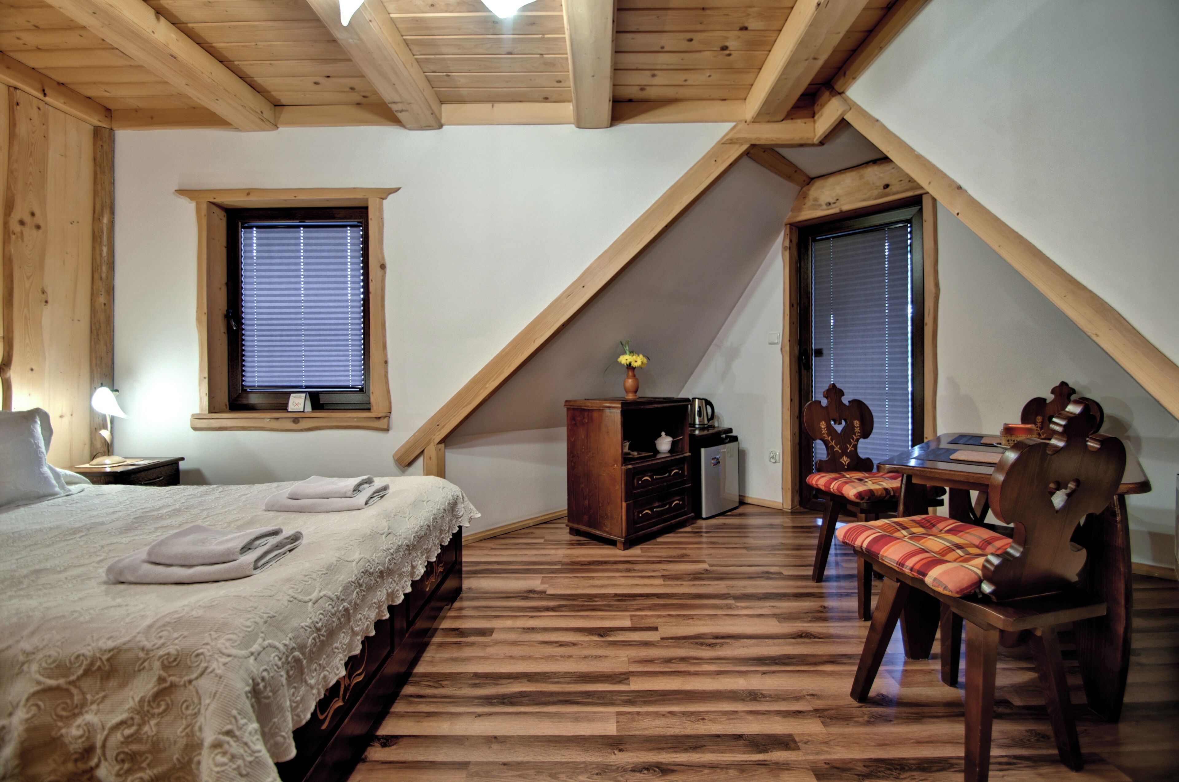 A bedroom with a bed, a dresser, a table with chairs, and a window with blinds.
