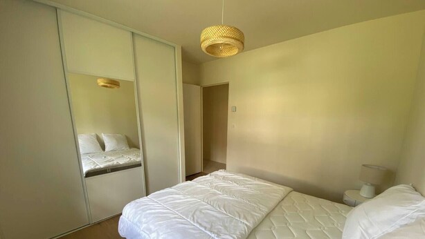 Ein Schlafzimmer mit Bett, Nachttisch, Lampe, Spiegel und Kleiderschrank.