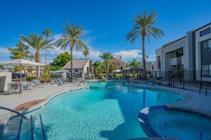 A swimming pool with lounge chairs and umbrellas, surrounded by palm trees and modern buildings. - Sunny Scottsdale Retreat with  Pool, Gym & Parking (Scottsdale)