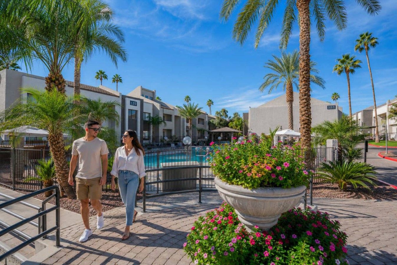 A hotel with a pool, palm trees, and a paved walkway.