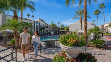 A hotel with a pool, palm trees, and a paved walkway.