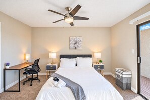 A hotel room with a bed, two bedside tables with lamps, a desk with a chair, a ceiling fan, and a large window. - Sunny Scottsdale Retreat with  Pool, Gym & Parking (Scottsdale)