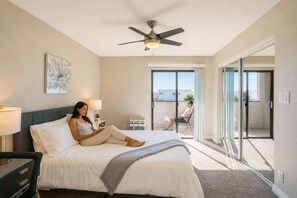 Une chambre d’hôtel avec un lit, un ventilateur de plafond, une grande fenêtre et une porte-fenêtre coulissante donnant sur un balcon.
