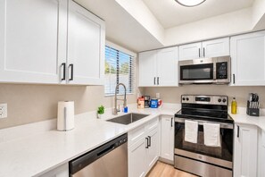 A modern kitchen with white cabinets, a stainless steel microwave, an oven, and a dishwasher.