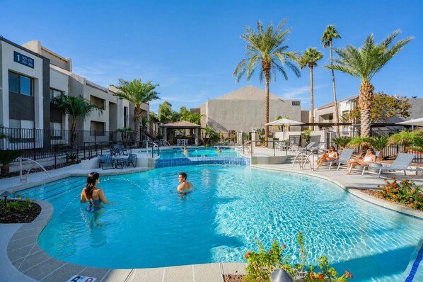 Une piscine avec des chaises longues, des palmiers et un bâtiment sur lequel est affiché un panneau indiquant les numéros des chambres.