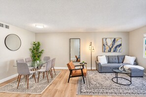 A modern living room with a grey sofa, a dining table with chairs, a large mirror, and a floor lamp. - Sunny Scottsdale Retreat with  Pool, Gym & Parking (Scottsdale)