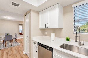 A modern kitchen with white cabinetry, a dishwasher, a sink with a faucet, and a dining area with a table and chairs. - Sunny Scottsdale Retreat with  Pool, Gym & Parking (Scottsdale)