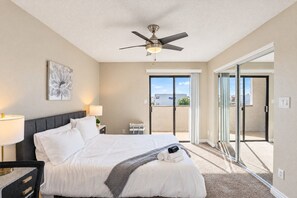 A hotel room with a bed, a ceiling fan, a nightstand with a lamp, a painting on the wall, and a sliding glass door leading to an outdoor area. - Sunny Scottsdale Retreat with  Pool, Gym & Parking (Scottsdale)