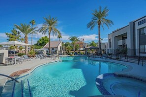 Une piscine entourée de bâtiments dotés de balcons, avec des chaises longues et des palmiers.
