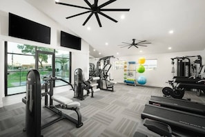 A gym with exercise equipment, large windows, and a ceiling fan.