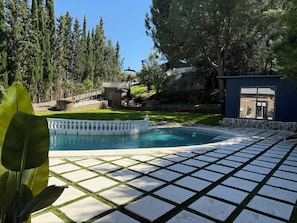 A swimming pool with a white fence, surrounded by stone tiles and greenery. - Charming mini house in Seville with jacuzzi (Guillena)