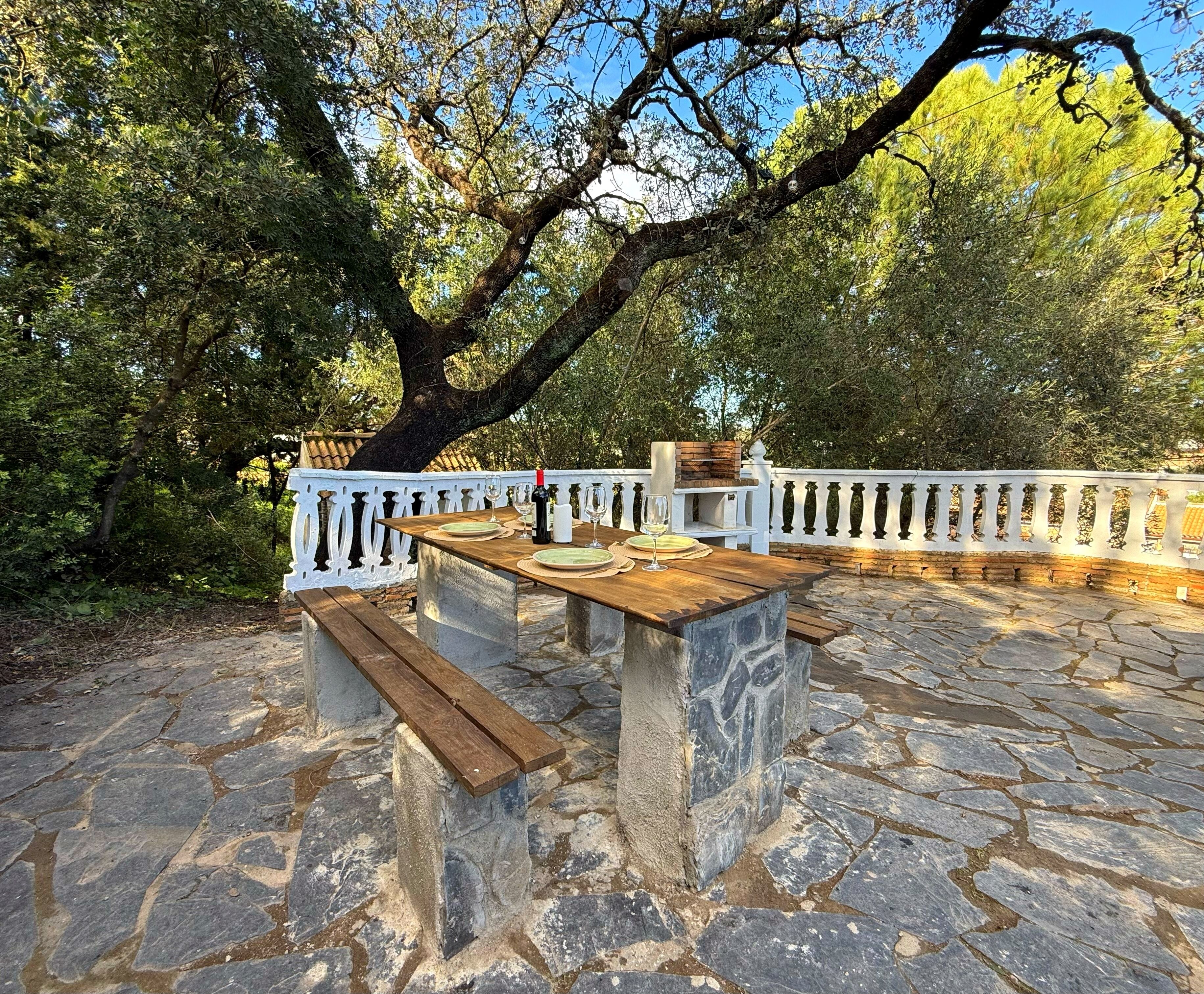 An outdoor dining area with stone flooring, a wooden table, and a white railing.