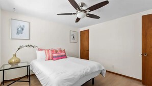 A bedroom with a bed, a ceiling fan, a nightstand with a vase, and two doors.