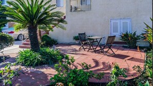 A patio with a table and chairs, surrounded by plants and a palm tree.