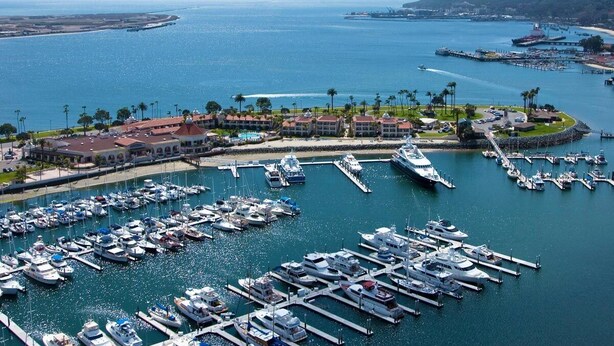 A marina with numerous boats docked, a large building with a red roof, and a clear view of the surrounding coastline.