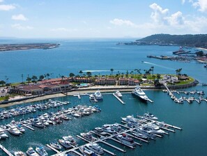 A marina with numerous boats docked, a large building with a red roof, and a clear view of the surrounding coastline.