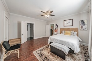 A bedroom with a large bed, a ceiling fan, and a door leading to another room.