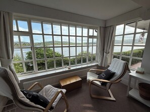 A room with large windows, two chairs, a small table, and a view of a body of water. - Benarth Lodge a charming unique hideaway in Conwy (iverside Business Park)