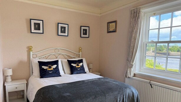 A bedroom with a bed, bedside tables, a window with curtains, and framed pictures on the wall. - Benarth Lodge a charming unique hideaway in Conwy (iverside Business Park)
