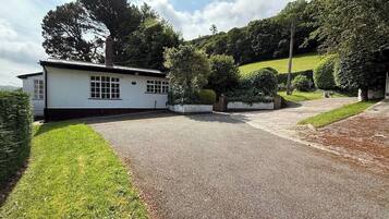 A white building with a gravel driveway, surrounded by greenery and hills.