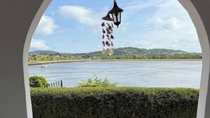 A patio with two white chairs and a table, overlooking a river with a boat and greenery in the background. - Benarth Lodge a charming unique hideaway in Conwy (iverside Business Park)