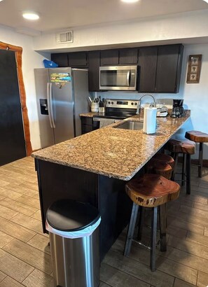 A modern kitchen with granite countertops, stainless steel appliances, and wooden bar stools.