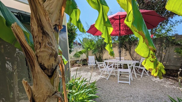 A patio area with a white table and chairs, surrounded by gravel, and a red umbrella providing shade.