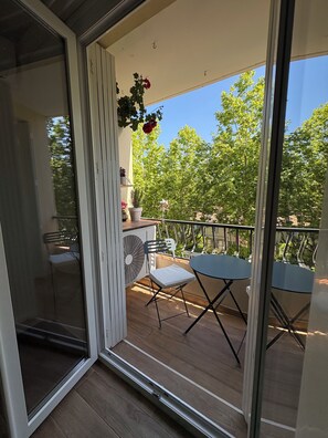 Un balcon avec une table et des chaises, un pot de fleurs et une vue sur les arbres.