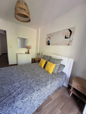Une chambre à coucher avec une couvre-lit à motifs, une lampe de chevet, un miroir et une œuvre d’art murale.