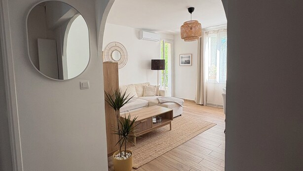 Ein Zimmer mit Holzboden, einer Couch, einem Couchtisch, einem Spiegel und einer Pendelleuchte.