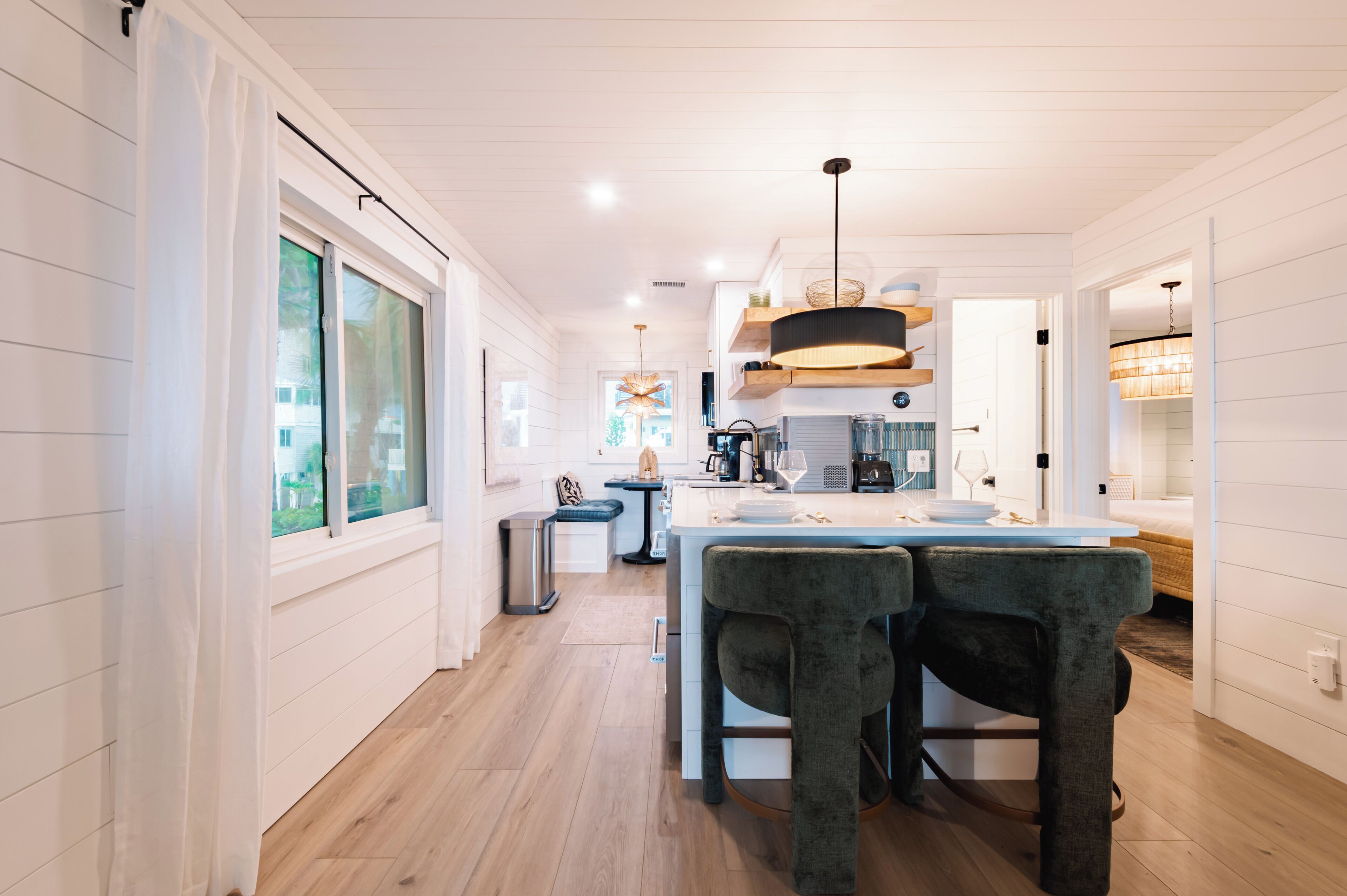 A modern kitchen with a central island, wooden flooring, and pendant lighting.