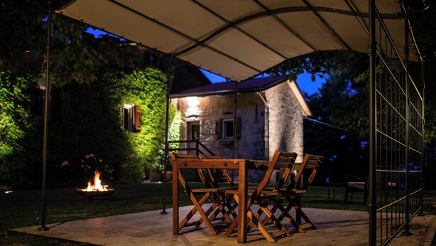 An outdoor patio area with a table and chairs under a canopy, a fire feature, and a stone building in the background. - Podere Monte, panoramic terrace on the Apennines with walks and barbecues. (Gaggio Montano)