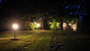 A nighttime outdoor area with a well-lit pathway, trees, and a building with a stone wall. - Podere Monte, panoramic terrace on the Apennines with walks and barbecues. (Gaggio Montano)