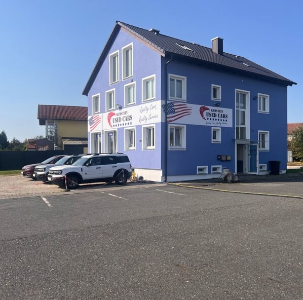 A two-story building with a sign for 'Hamstein Used Cars' and a parking lot with several cars. - Vilseck Stay (Vilseck)