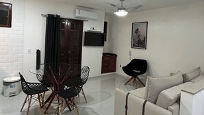 Una sala de estar moderna con comedor, un sofá, un ventilador de techo y un televisor montado.